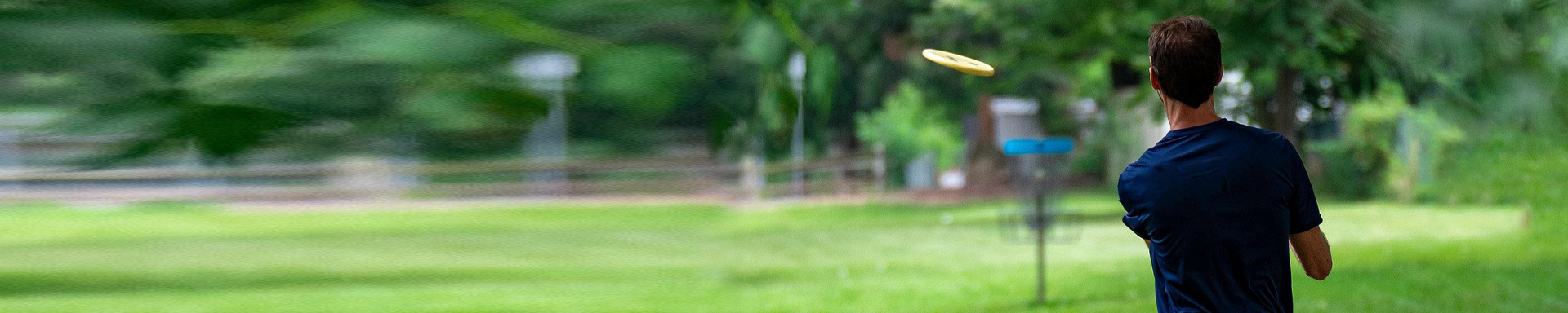 Henkilö heittämässä keltaista frisbeetä frisbeegolf koriin.