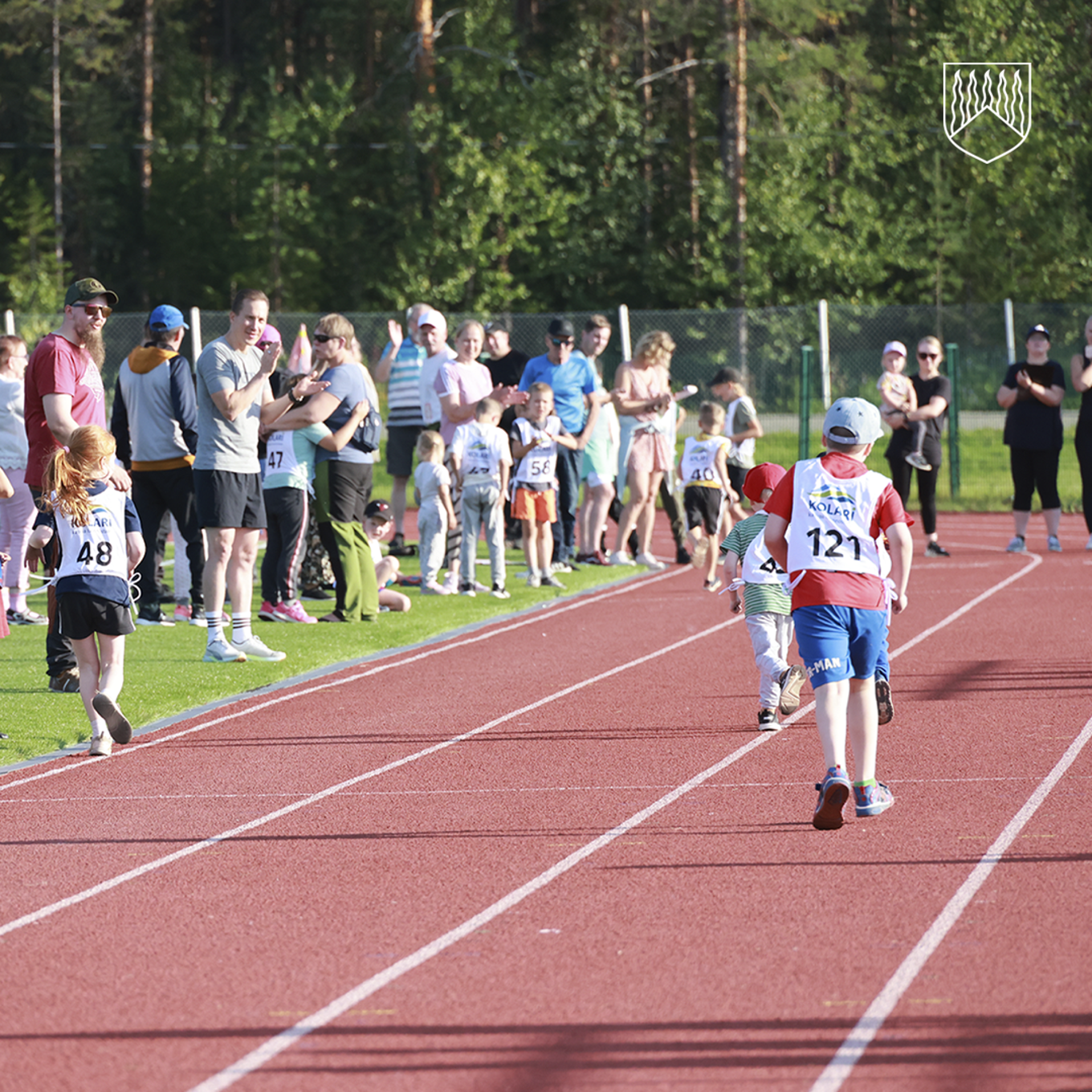 Sarjajuoksut urheilukentällä 2024. Lapset juoksevat ja yleisö kannustaa.
