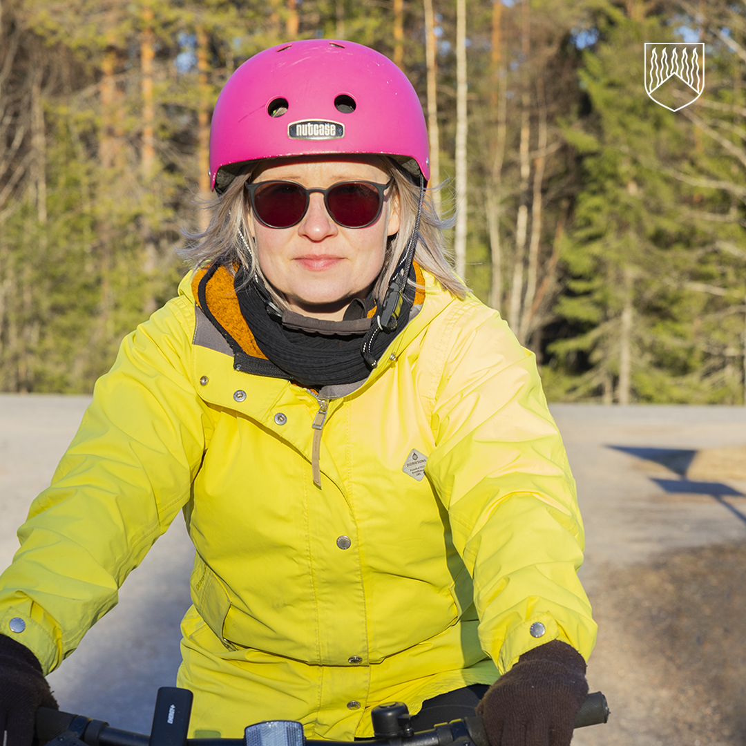 Pyöräilijä ajaa metsämaisemassa aurinkoisena päivänä. Pyöräilijällä on huomiovärinen takki, kypärä ja aurinkolasit.